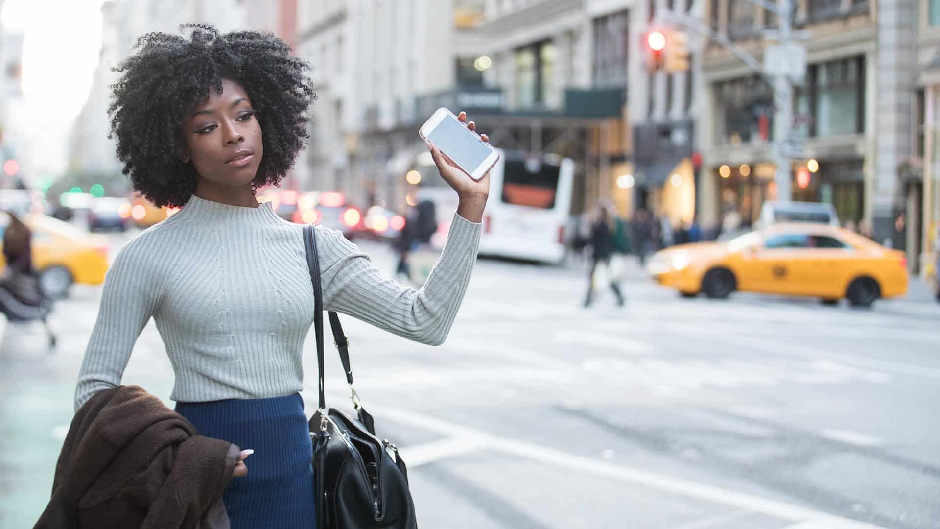 woman holding a rideshare app and waiting for her ride to arrive