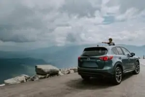 A car on the top of a hill with a boy pointing out of the sun roof.