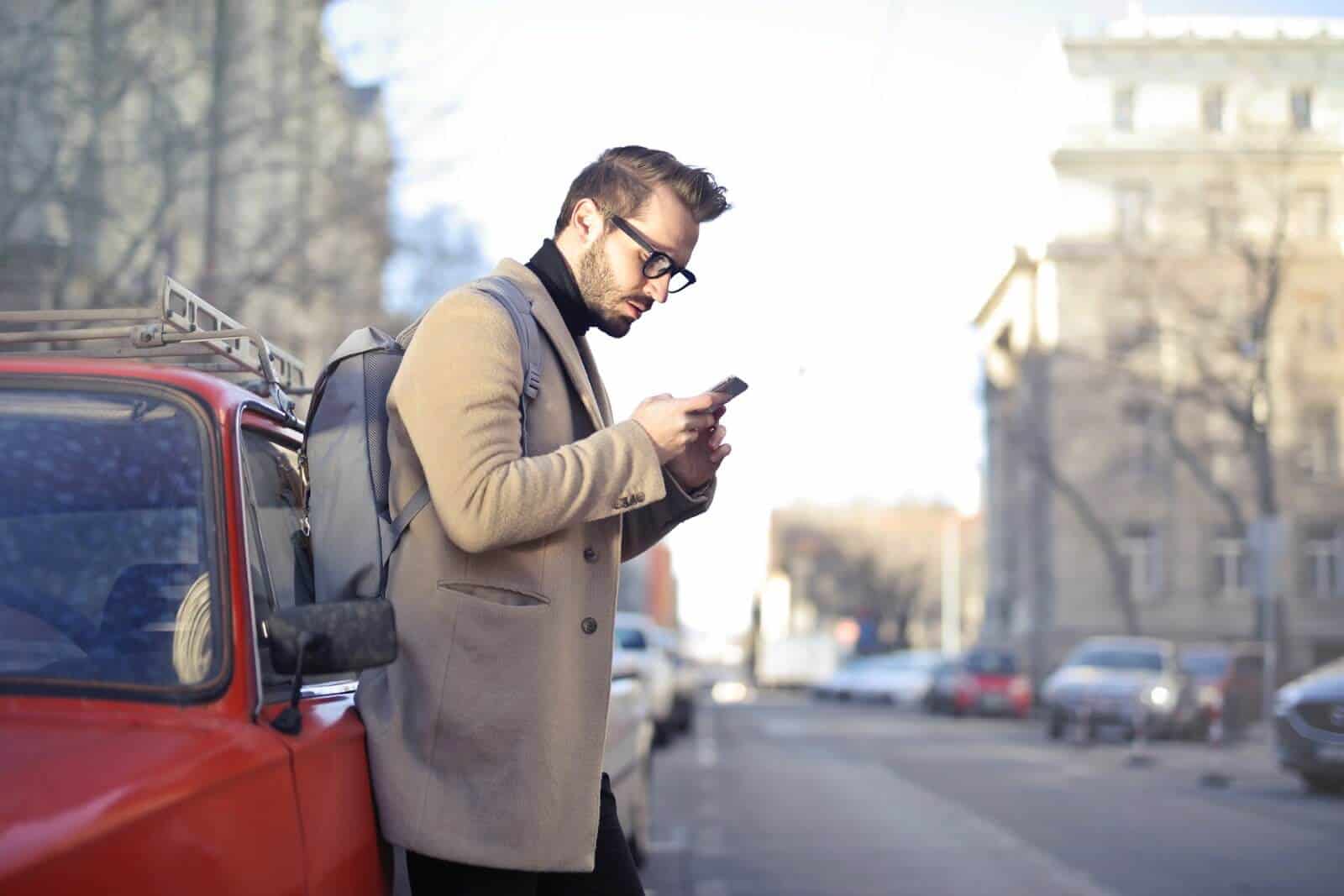 Man next to a car in beige coat holding phone