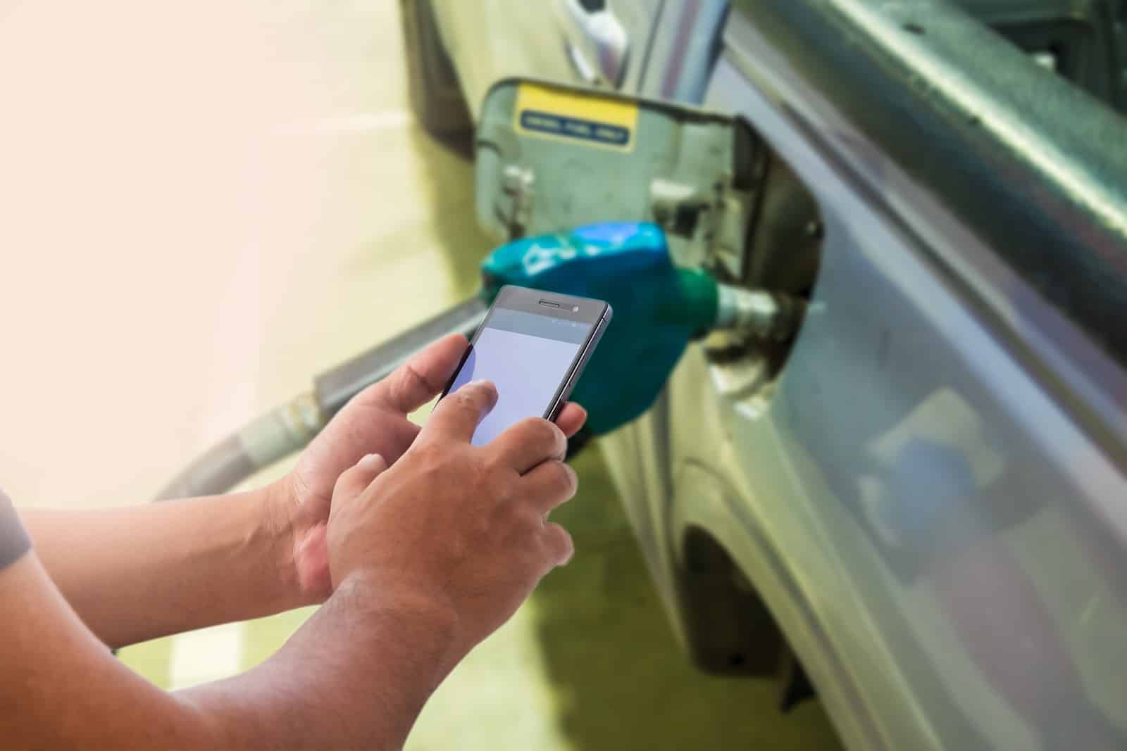 Person typing on their phone while pumping gas