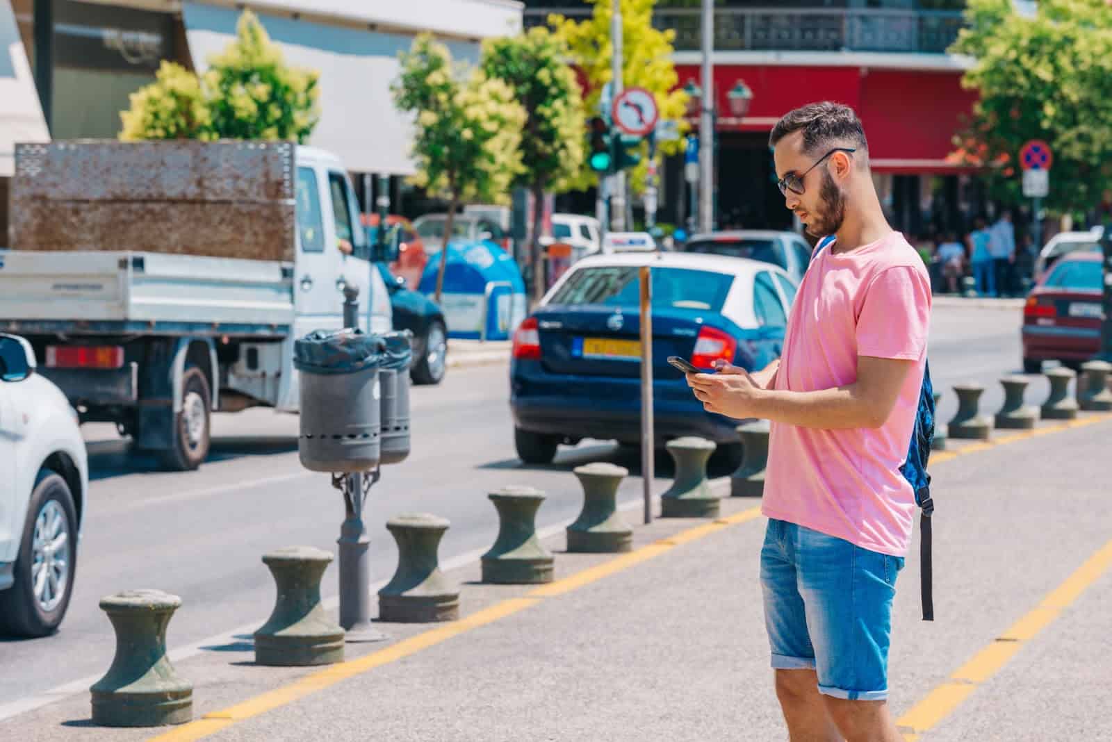 Lyft Ride Pass: A man waits by the side of the road, watching his phone screen for updates on his Lyft ride