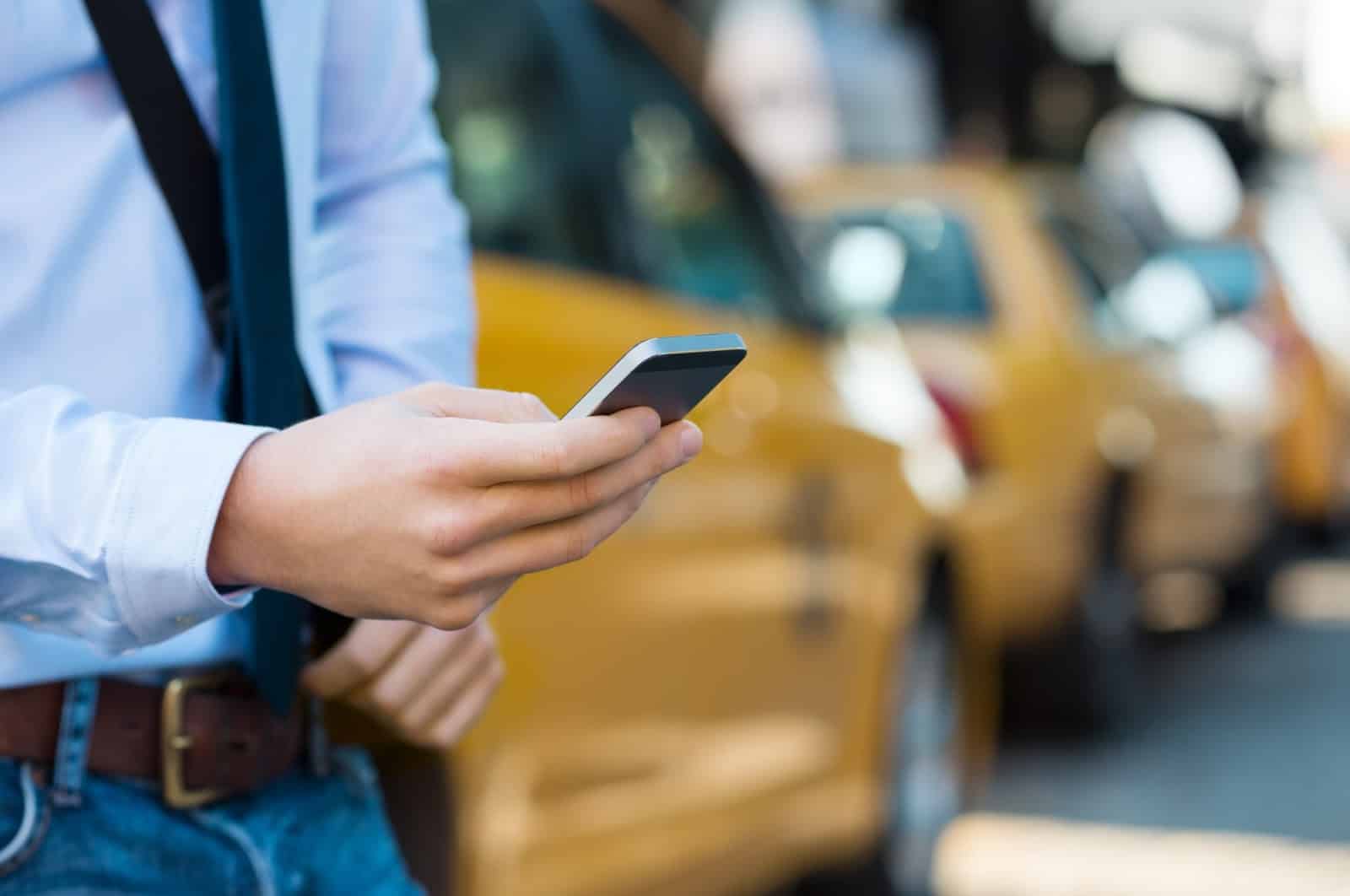 Curb promo code: A person uses his smartphone with taxis in the background