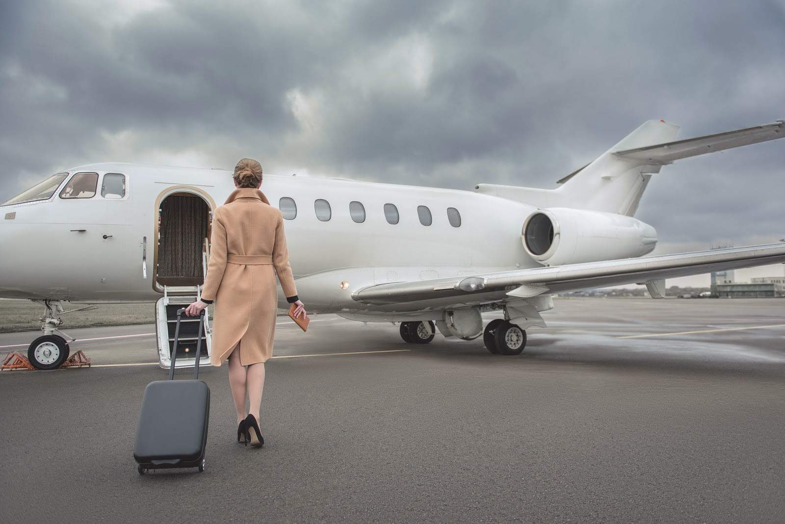 A woman walks up to a private jet with her suitcase