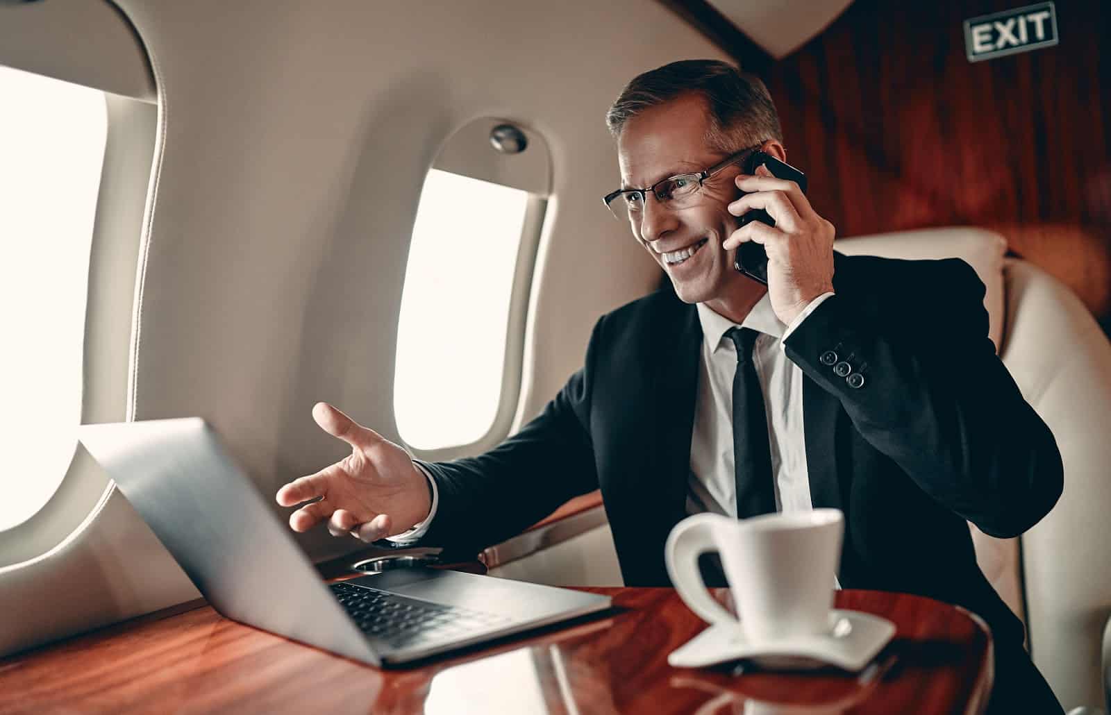 What is a chartered flight: A smiling business man gestures at his laptop on a private plane