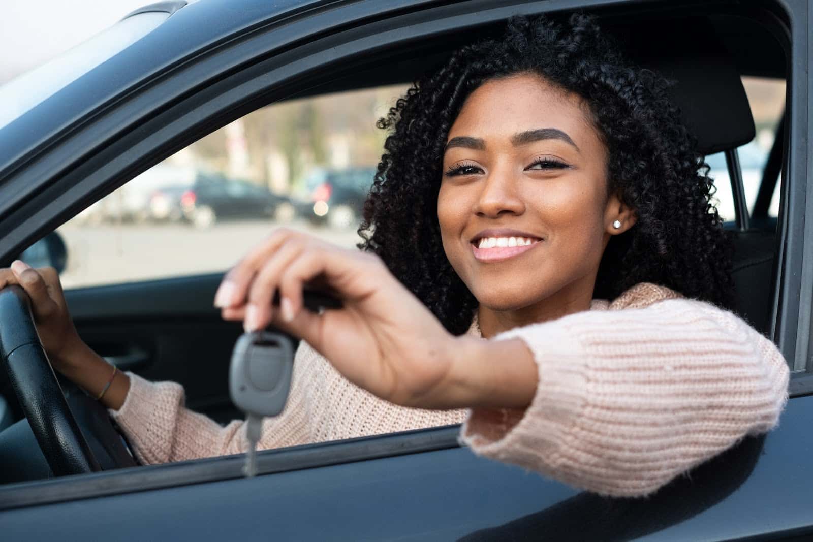Smiling woman holds keys while sitting in driver's seat