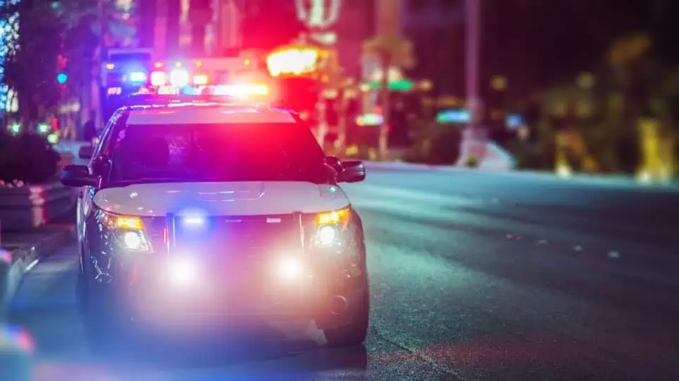 image showing a police vehicle with its lights on in a street - header graphic for can you drive for Uber with a DUI post on ridester.com